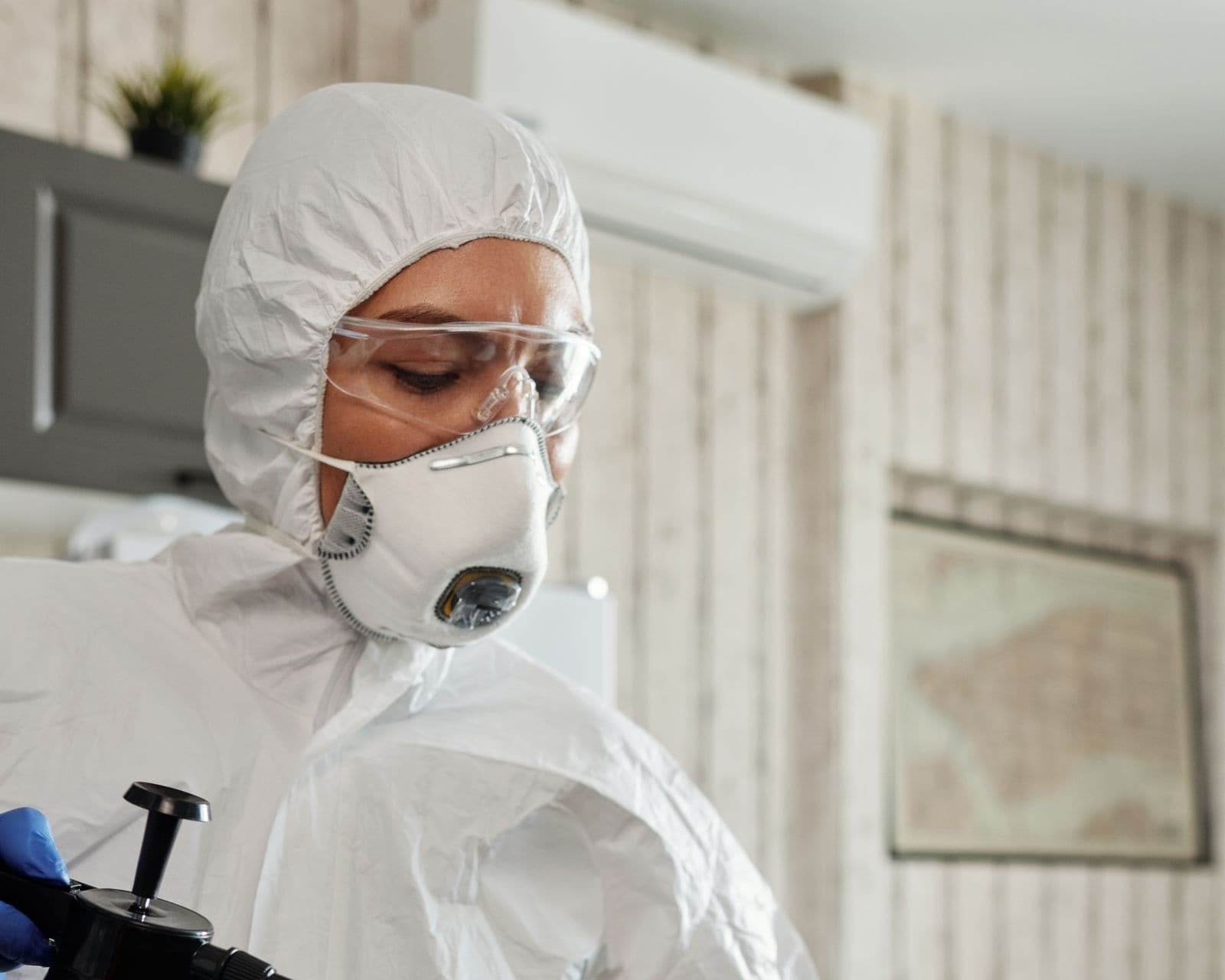 Personne en combinaison de protection intégrale procédant à la désinfection de surfaces intérieures.