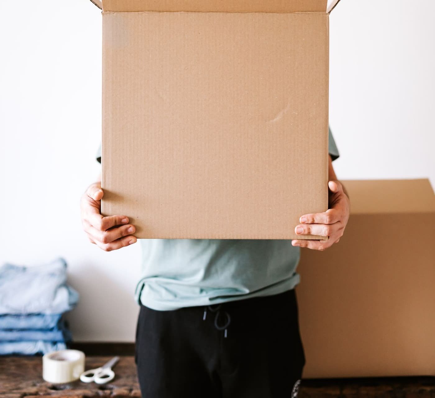 Personne portant un carton ouvert dans un logement en cours de vidage. Aucun visage visible.